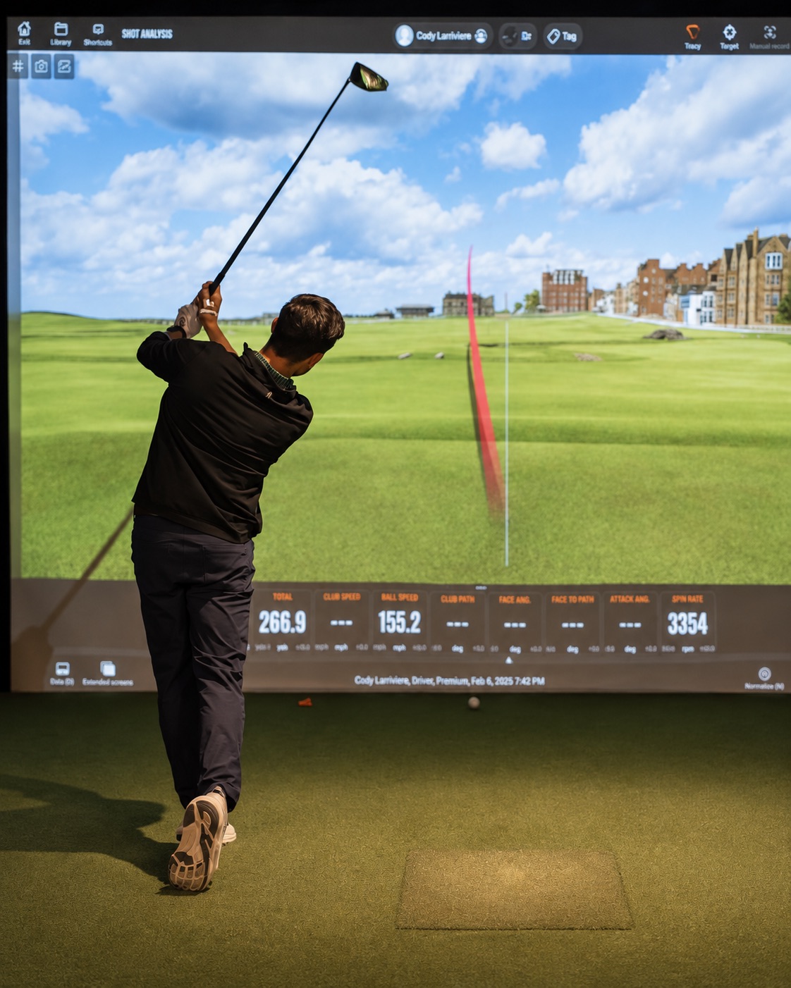 A golfer follows through on a shot at The Hideout, with the ball flight displayed on the simulator screen.